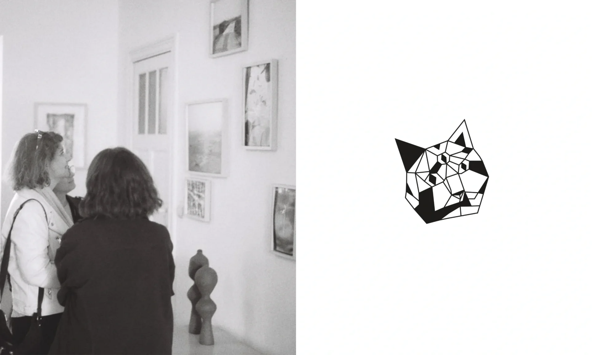 Black and white film photograph of the living room where the exhibition took place. There are photographs on the wall, ceramics displayed on a table, and three people looking at the artwork.