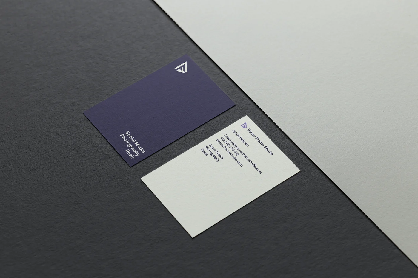 Front and back of a business card designed for Power Frame Studio. The front is light-colored while the back is dark-colored, and there is text specifying all the contact information of the company.